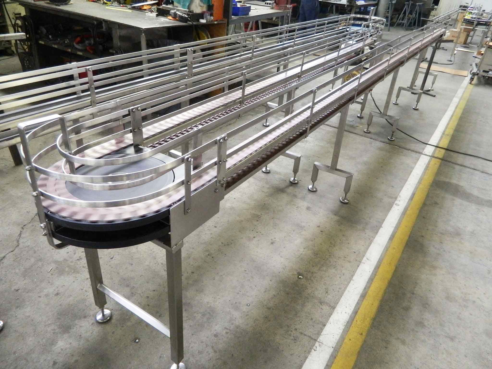 Stainless steel conveyor system with multiple tracks, showcasing its assembly in a workshop, highlighting industrial design and functionality.